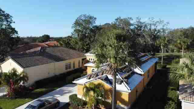 A tile roof under construction. Most of the home is blocked by a palm tree, so only certain sides are visible